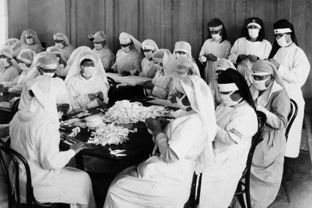 Volunteer caregivers from the American Red Cross during the 1918 flu epidemic sit round a table wearing personal protective equipment made of reusable material.