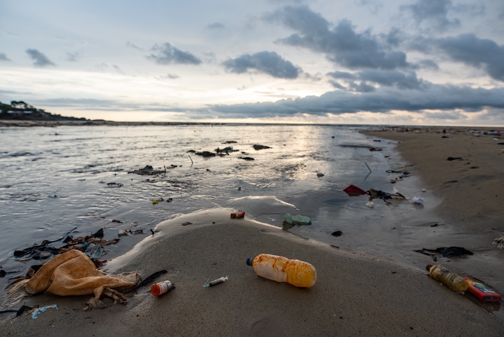 Broken syringe and pill bottle on a beach