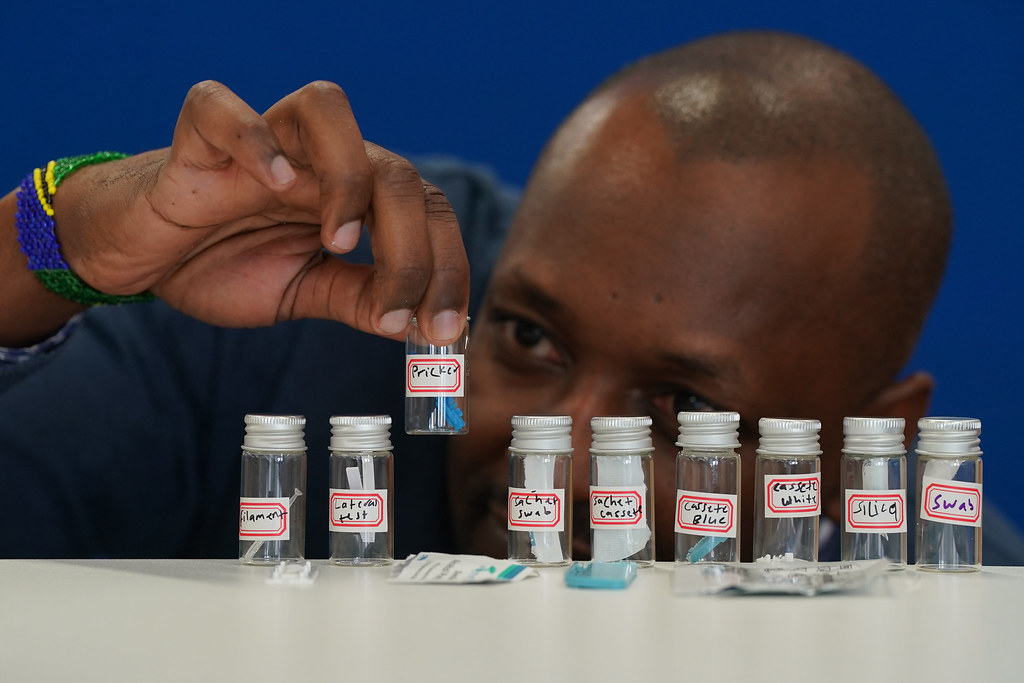 A researcher holds up one of several bottles containing parts of a Malaria RDT kit.