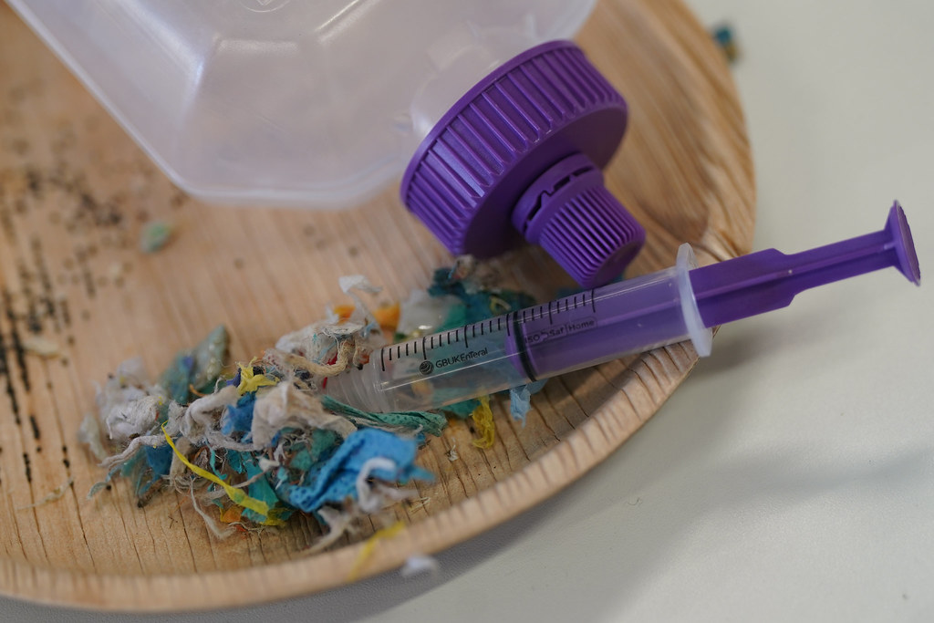 A plastic syringe lies next to other plastic medical waste including a enteral feeding bottle