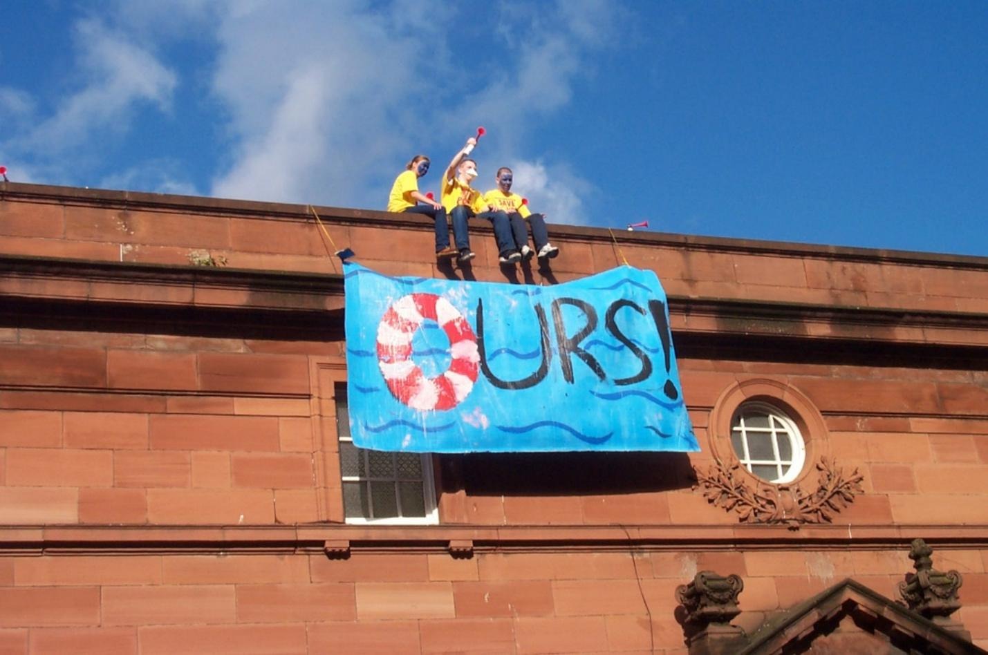 Three community activists occupy Govanhill baths, sitting on the roof of the baths with a banner that reads 'Ours' in 2001 when the pool was threatened with closure