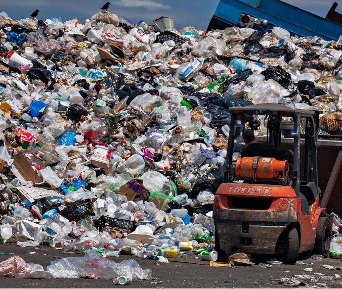 A large wall of waste is being moved around by an orange forklift truck digger.