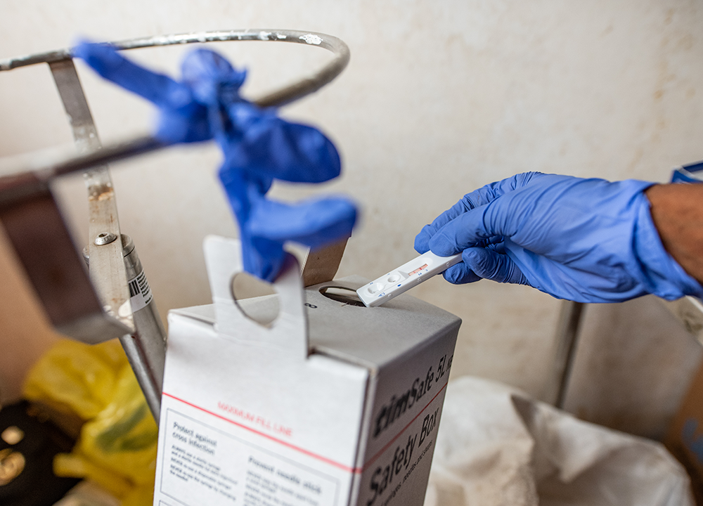 A hand in a blue glove puts a single use medical device into a box after use.