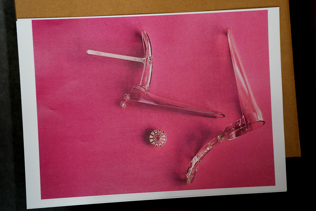 A deconstructed speculum on a 'feminine' pink background.