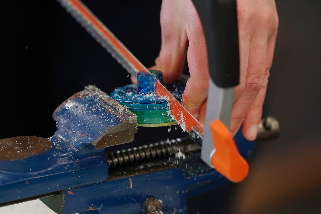 A team member uses a saw and clamp to cut a plastic component in half.