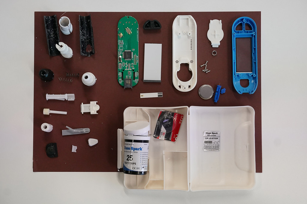 A deconstructed glucometer with all of the individual component parts laid out.