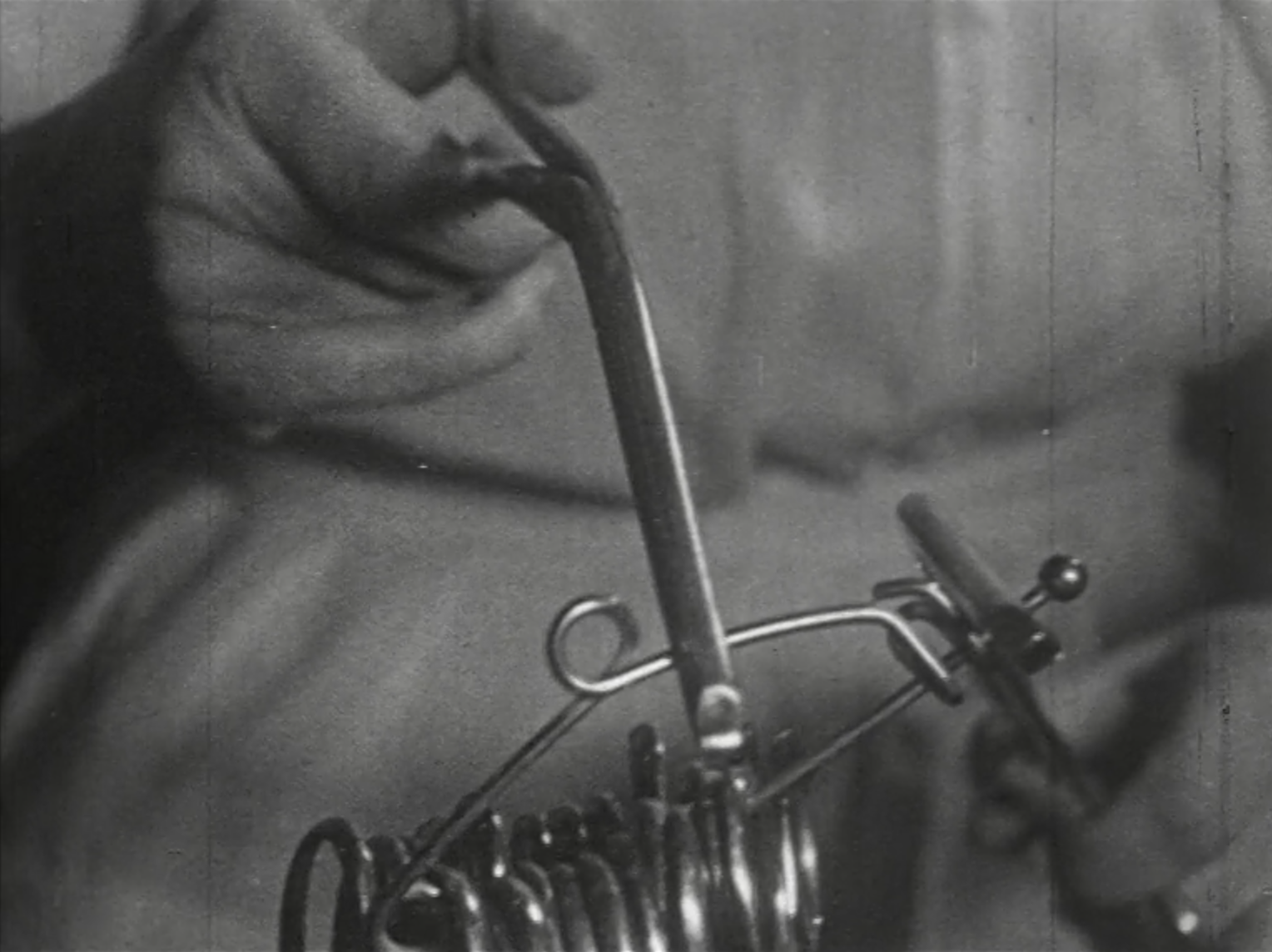 A black and white still from the film shows a hand gripping a metal medical tool. 