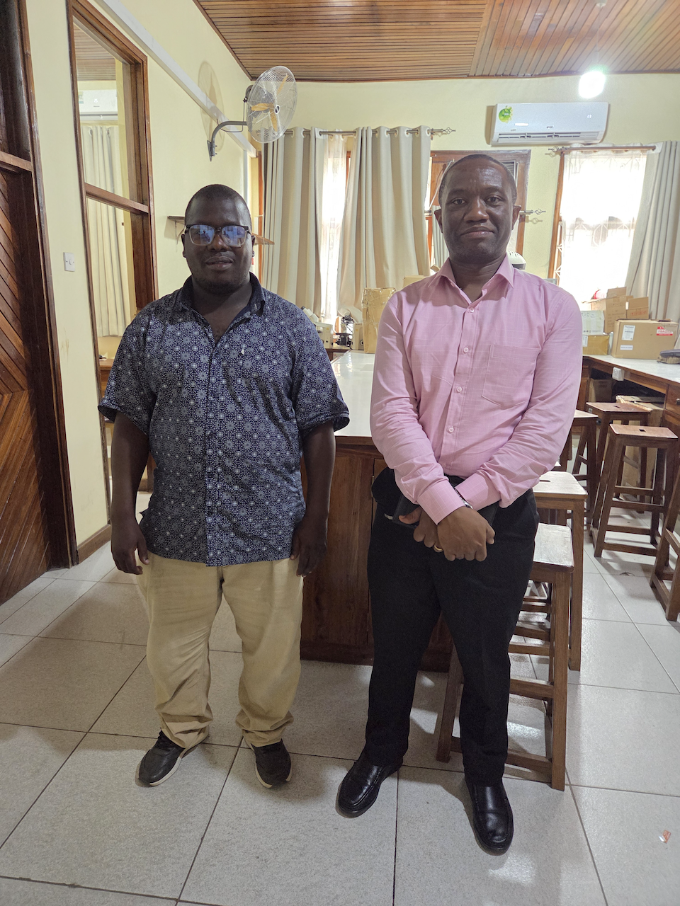 Researcher Peter Mangesho stands with a representative of the biomedical engineering unit, he is wearing a pink short and black trousers. 