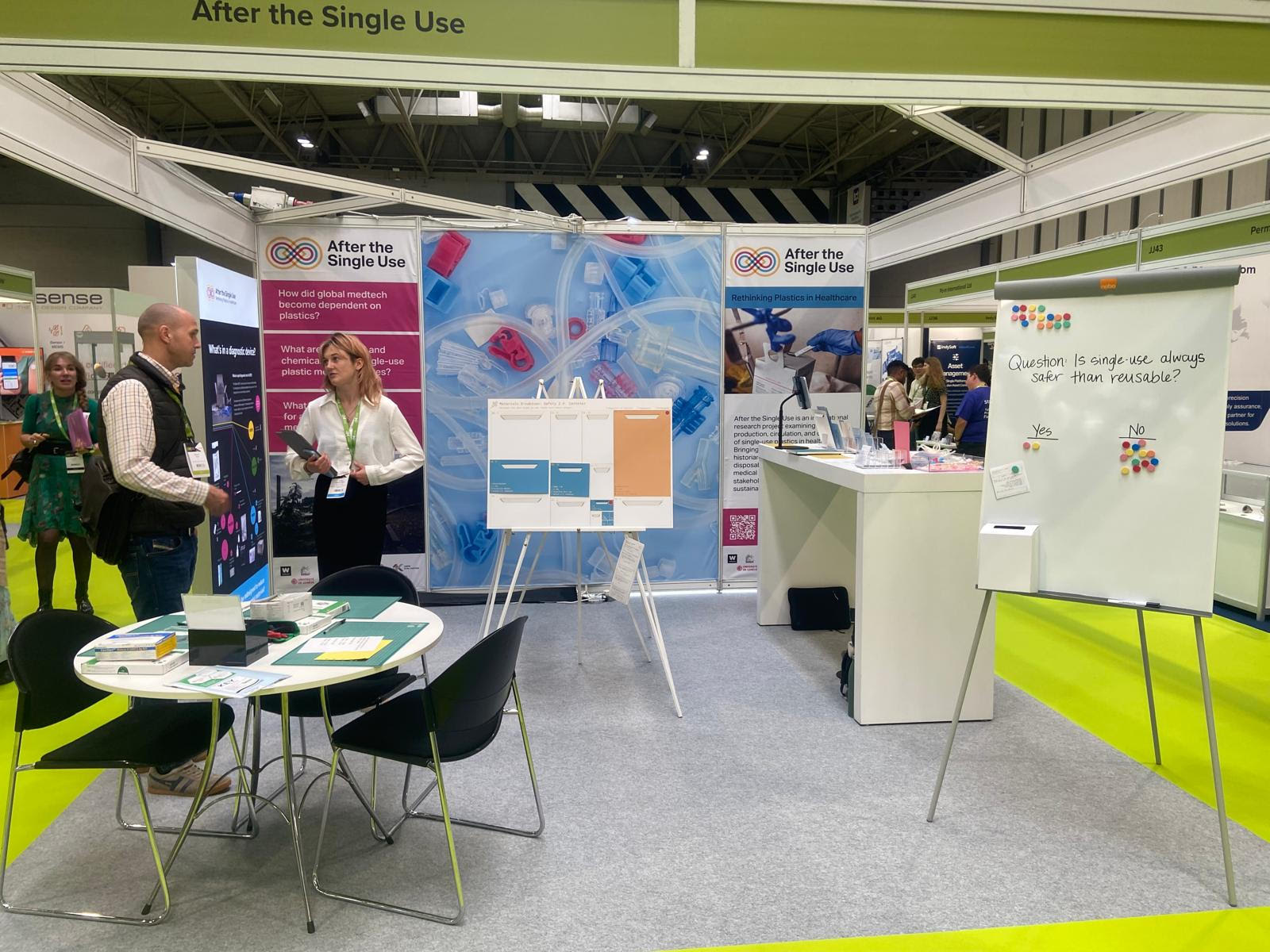 A conference exhibition space is shown with two people engaging in conversation and tables and displays showing the After the Single Use project. 