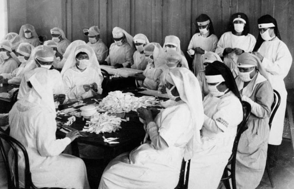 Volunteer caregivers from the American Red Cross during the 1918 flu epidemic sit round a table wearing personal protective equipment made of reusable material.
