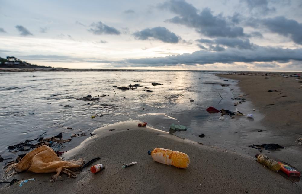 Broken syringe and pill bottle on a beach