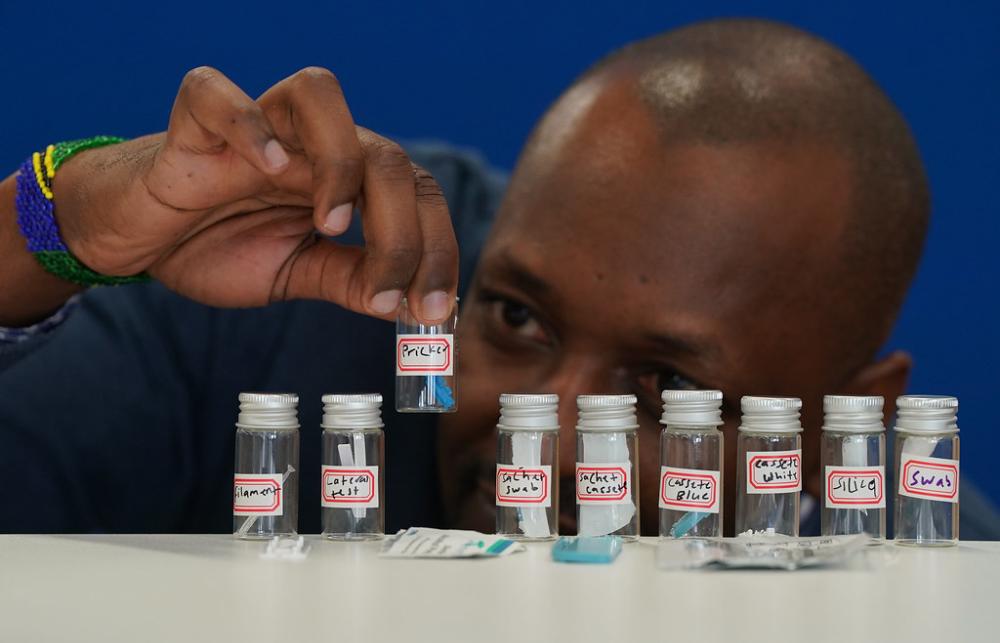 A researcher holds up one of several bottles containing parts of a Malaria RDT kit.