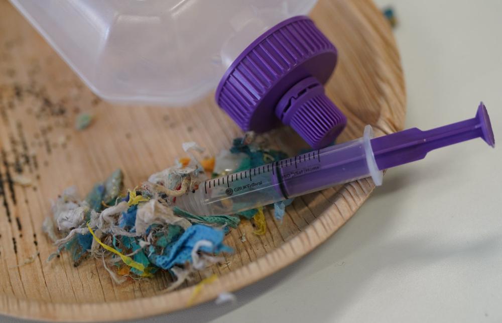 A plastic syringe lies next to other plastic medical waste including a enteral feeding bottle