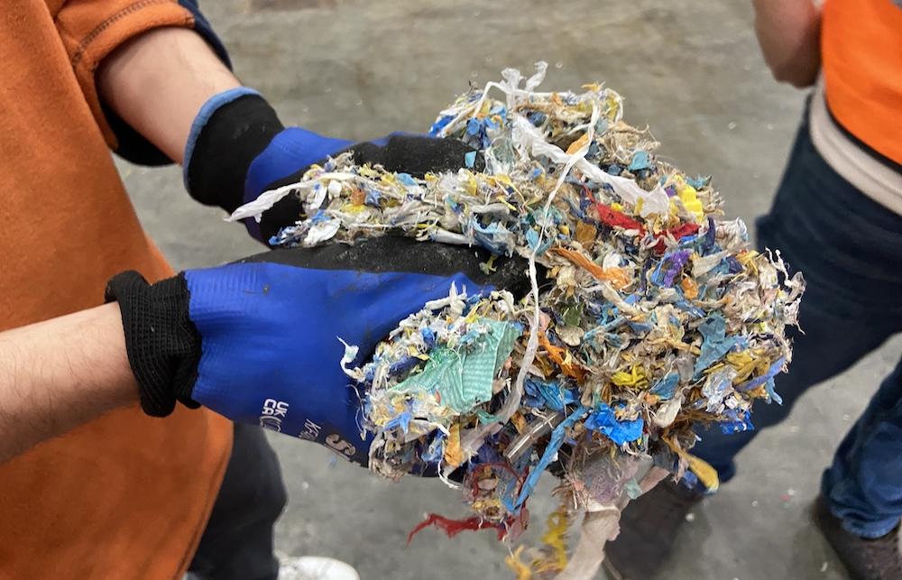 A waste disposal worker holds up two handfuls of plastic waste that cannot be recycled