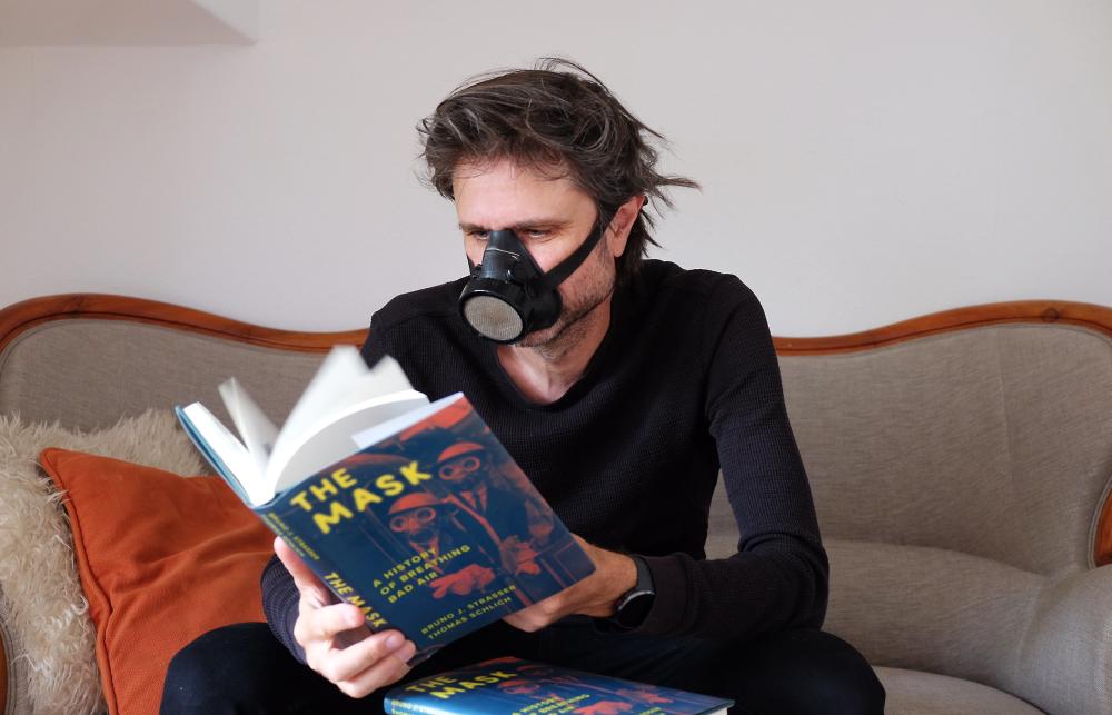 Bruno Strasser reading his book The Mask whilst wearing a mask.