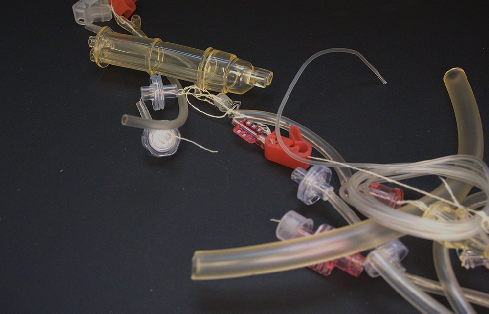 A disassembled single use medical device in placed on a table with a black background. 