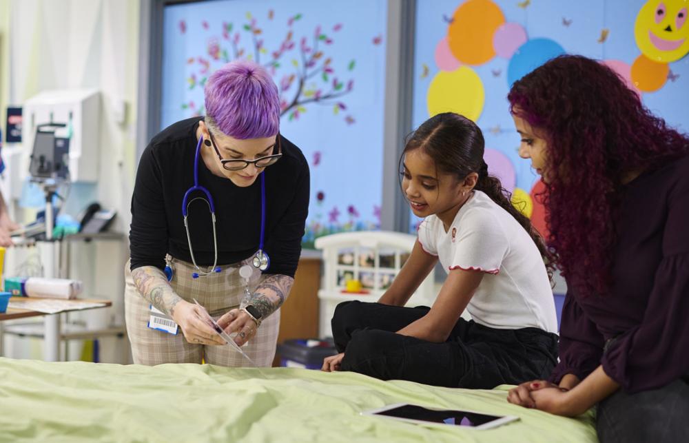 A healthcare professional and a child and adult are at a table in a hospital setting. 