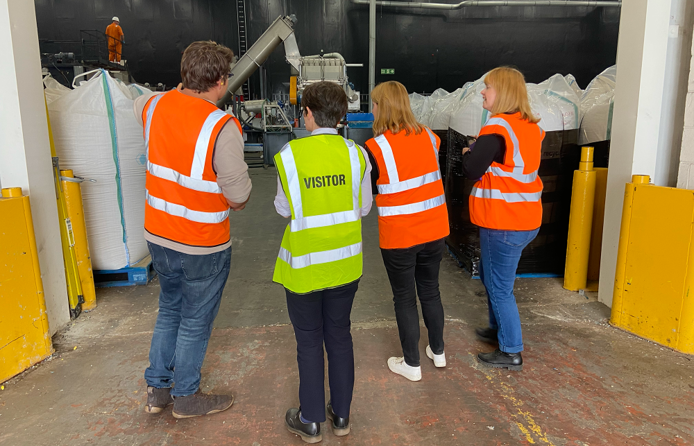Four people in hi-vis jackets stand in the foreground with large sacks of plastic waste in a warehouse space. 