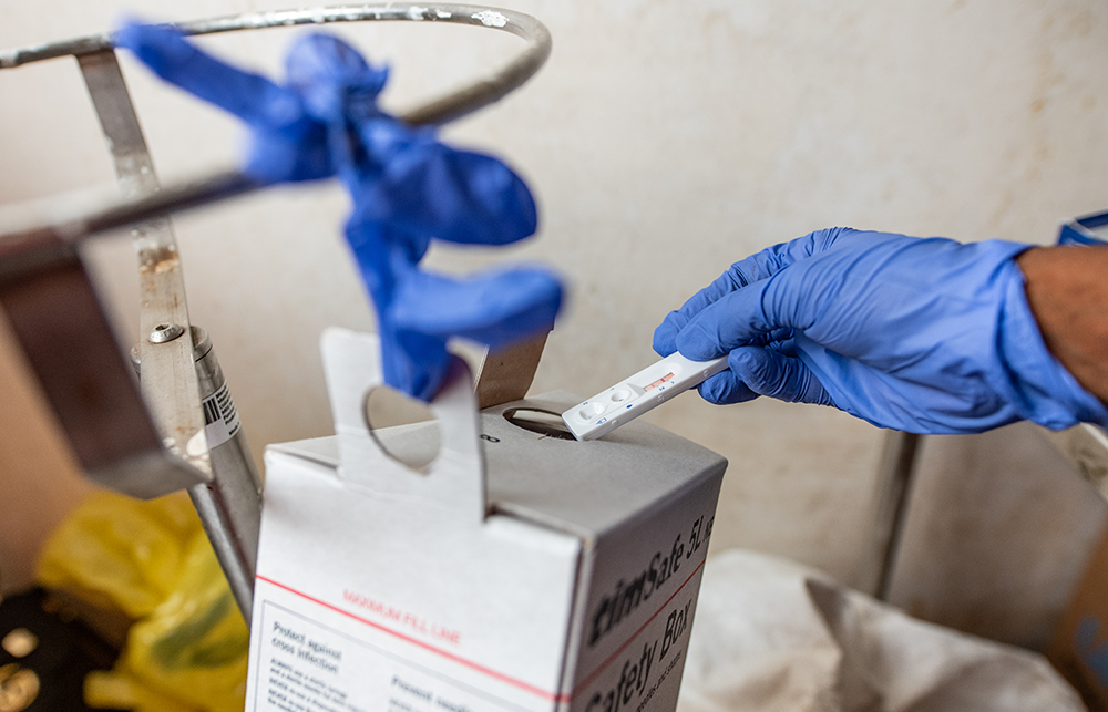 A hand in a blue glove puts a single use medical device into a box after use. 